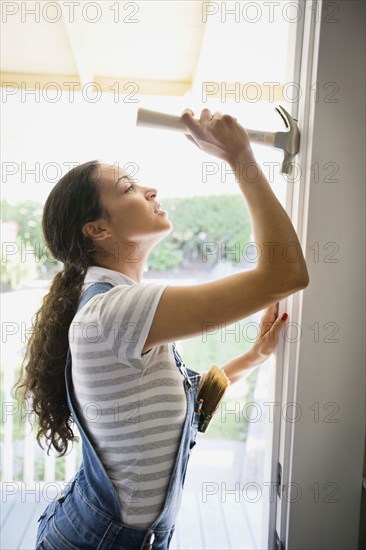 Mixed race woman removing nail from doorway