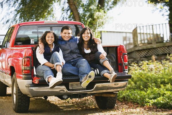 Hispanic siblings sitting in bed of truck