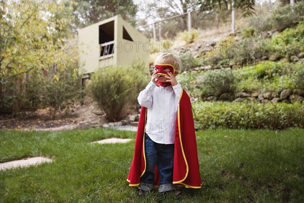 Boy wearing cape and mask in backyard