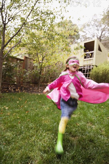 Middle Eastern girl wearing cape and mask running in backyard