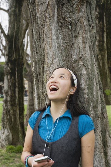 Chinese girl listening to headphones against tree