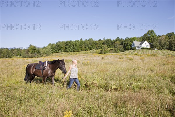 Caucasian woman leading horse through field