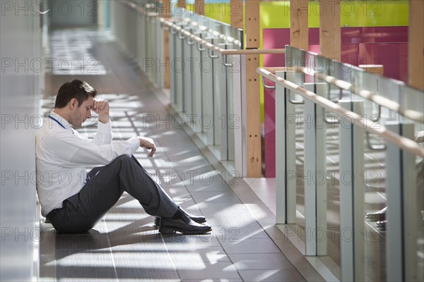 Frustrated businessman sitting on office corridor floor