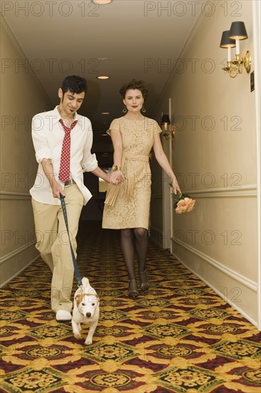 Young coupled dressed up walking down hotel hallway with dog