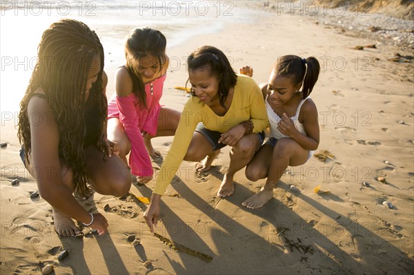 African American mother and daughters drawing on beach sand