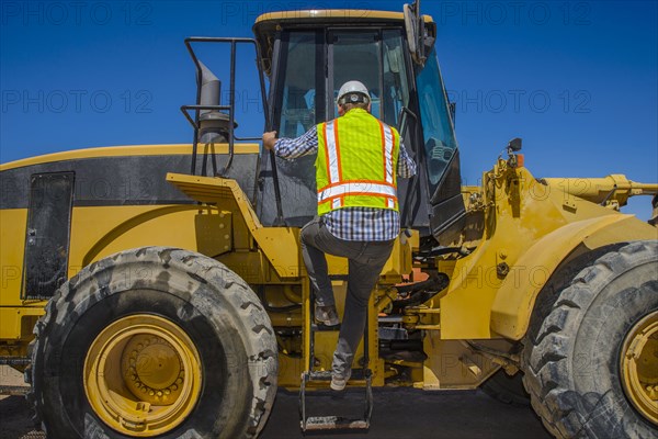 Caucasian construction worker climbing onto earth mover