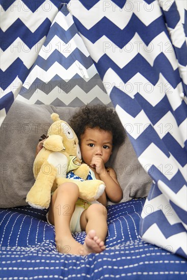 Mixed Race baby boy sucking thumb holding stuffed animal