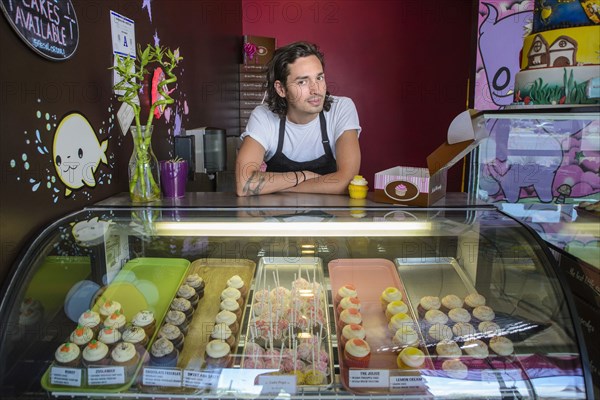 Hispanic business owner leaning on bakery display case