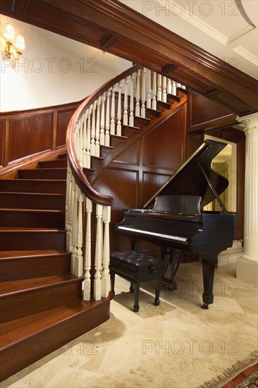 Baby grand piano at foot of large winding staircase