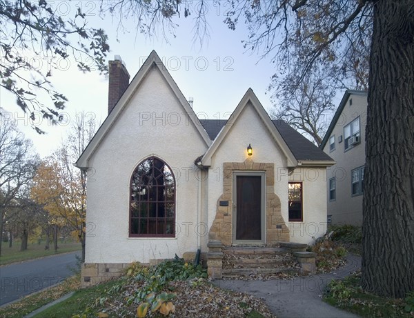 Front exterior view of white cottage with stone stairs and pointed rooftops