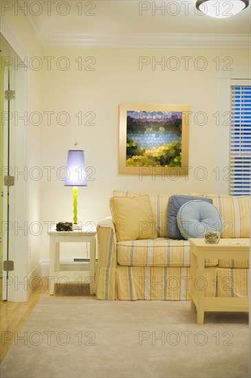 Purple lamp on end table near yellow and blue striped sofa