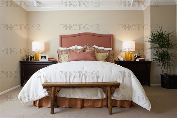 Arranged pillows on tidy bed with lit table lamps in the bedroom at home