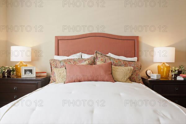 Arranged pillows on tidy bed with lit table lamps in the bedroom at home