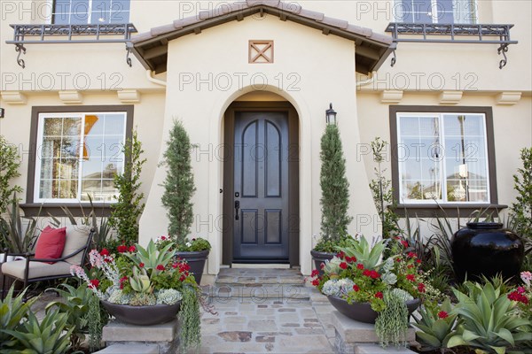 Walkway along plants leading to an arched entrance with closed brown door