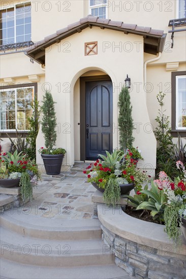 Walkway along plants leading to an arched entrance with closed brown door