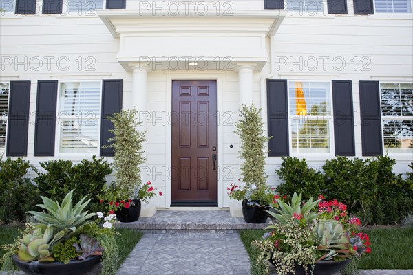 Walkway along plants leading to a house with closed brown door