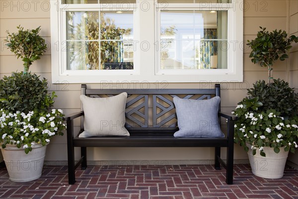 Brick flooring porch with bench and potted plants against the window