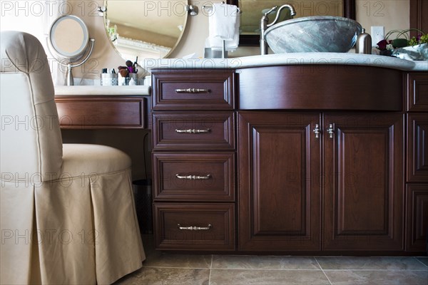 Chair with brown cabinets and mirrors in bathroom at home