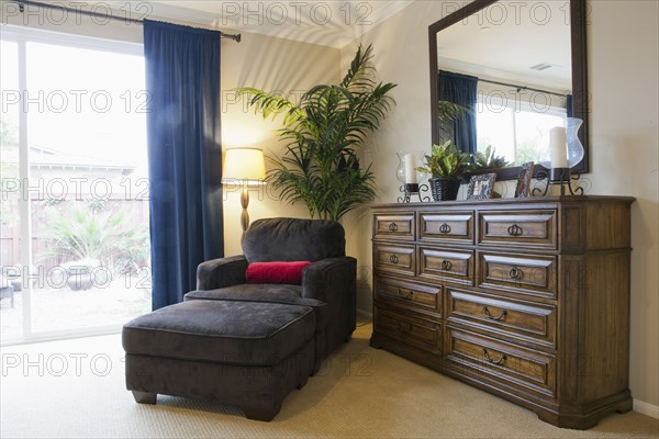 Armchair and ottoman by sideboard in bedroom