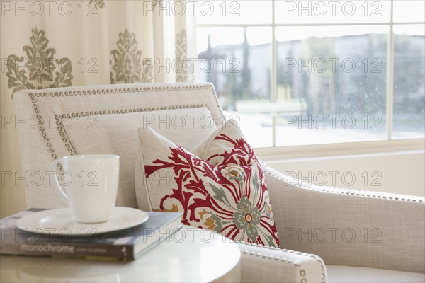 Close-up of tea cup with book besides armchair at home