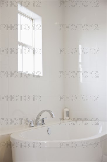 Close-up of a white bath with tiled wall and window in the bathroom