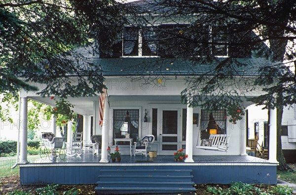 Pretty Summer cottage home with large front porch with columns. Porch all around. Dormer windows. American Flag