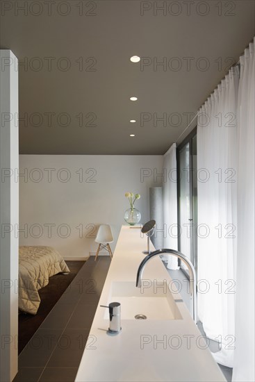 View of faucet and sink along curtained window and cropped bed at home