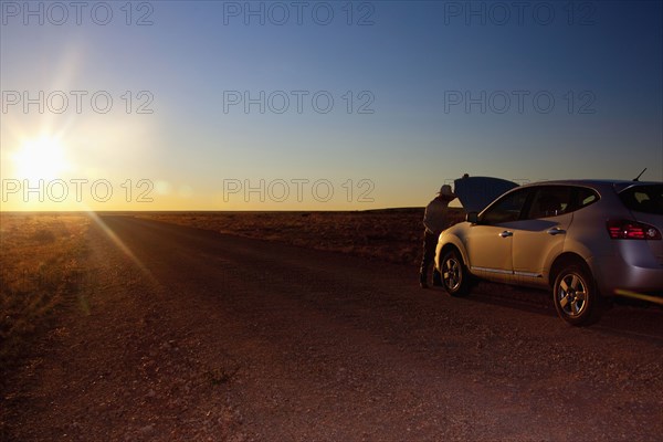 Person opening hood of car on remote road