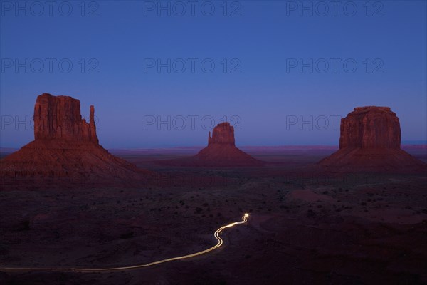 Long exposure of car driving past butte rock formations in desert landscape