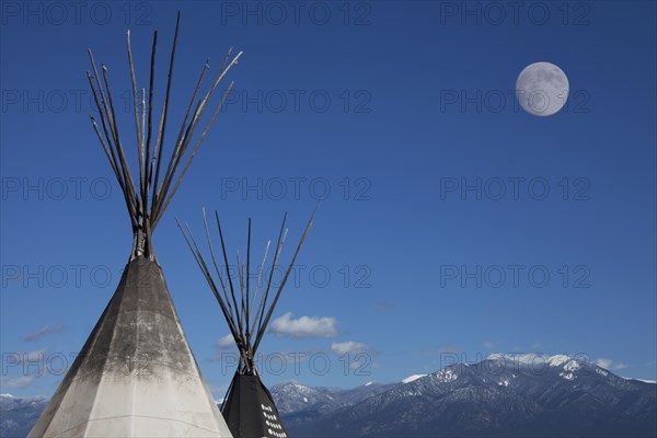 Teepees under full moon in blue sky