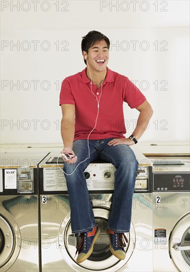 Asian man listening to mp3 player in laundromat