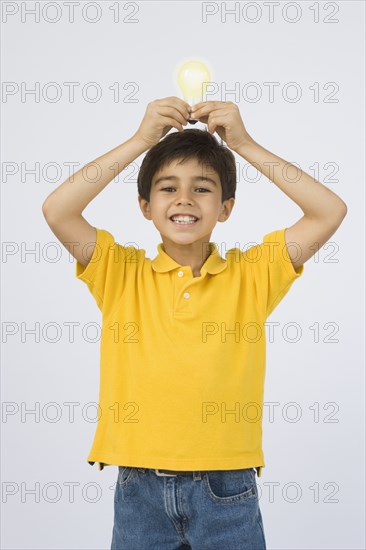 Middle Eastern boy holding light bulb over head