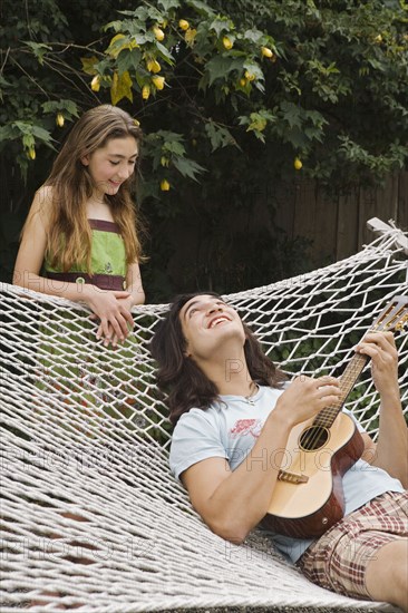 Pacific Islander man playing ukulele for sister