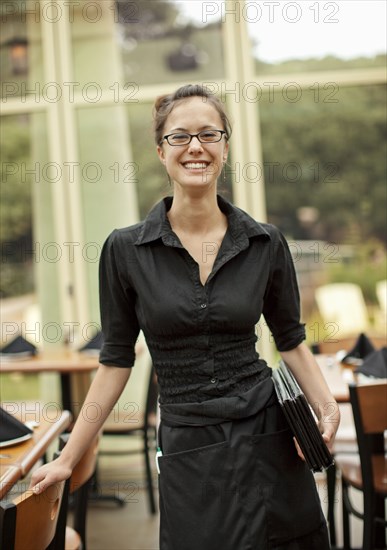 Portrait of smiling Hispanic waitress holding menus in restaurant