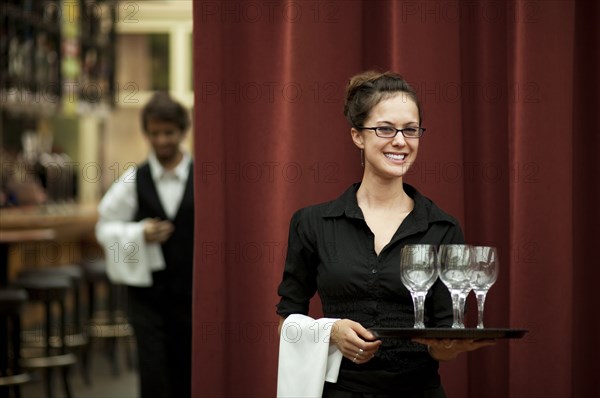 Smiling Hispanic waitress carrying tray of wine glasses