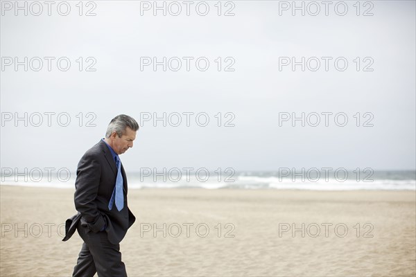 Pensive Hispanic businessman walking on beach