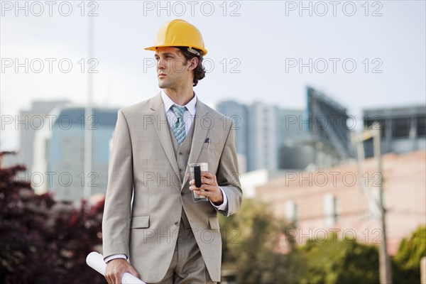 Hispanic businessman drinking coffee and carrying blueprint outdoors