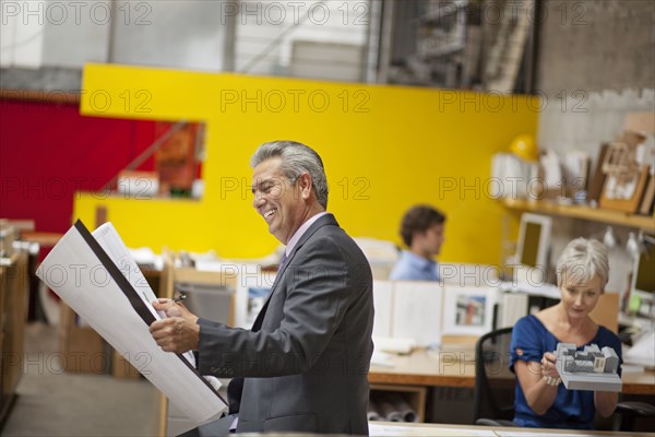 Smiling architect reading blueprint in office