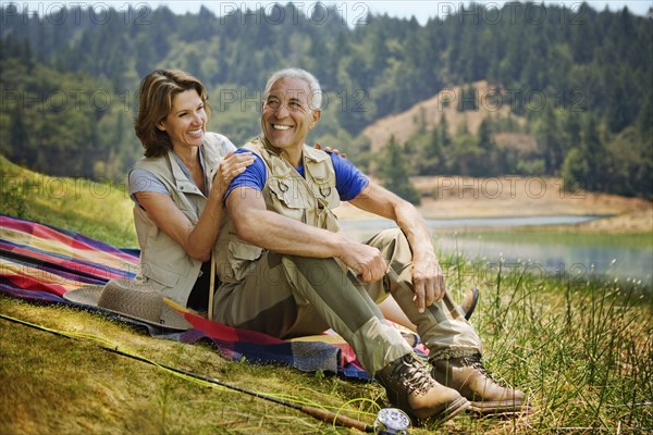 Couple sitting on blanket near lake with fishing rod
