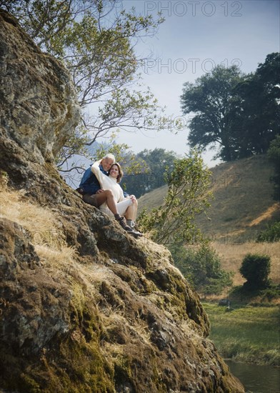 Caucasian couple sitting on hill near river