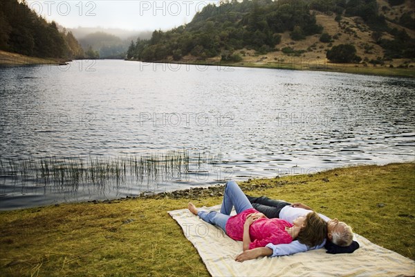 Couple laying on blanket near lake