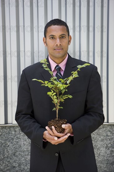 Serious mixed race businessman holding seedling
