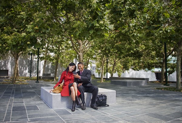 Businessman showing cell phone to businesswoman at park