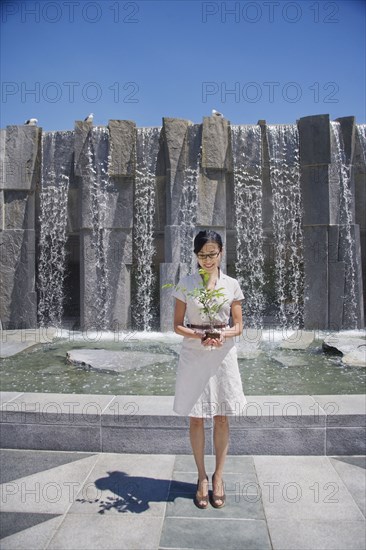 Asian woman holding seedling near fountain