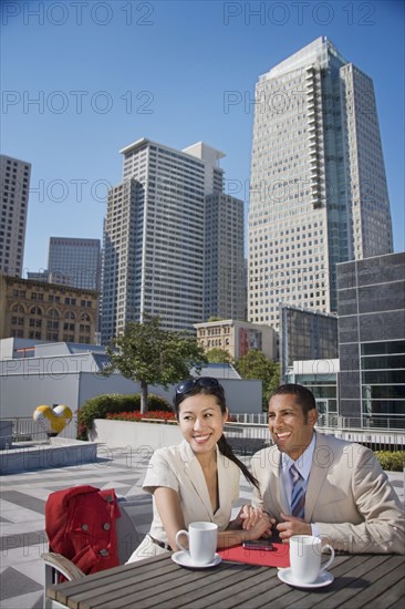 Smiling couple holding hands and drinking coffee outdoors