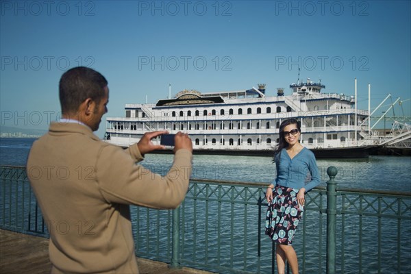 Man photographing woman at waterfront