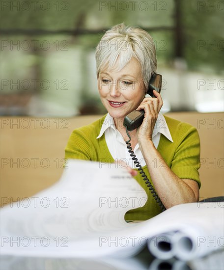 Caucasian architect talking on telephone and reading blueprint