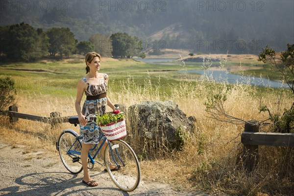 Smiling Hispanic woman standing with bicycle near river