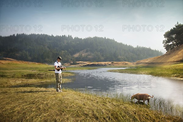 Caucasian man fishing in river near dog