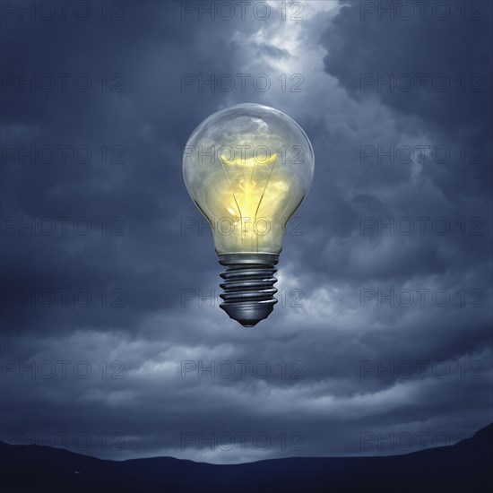 Illuminated light bulb floating in stormy sky